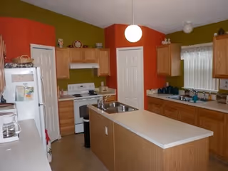 Bright kitchen with an island, wooden cabinets, appliances, and red and green walls.