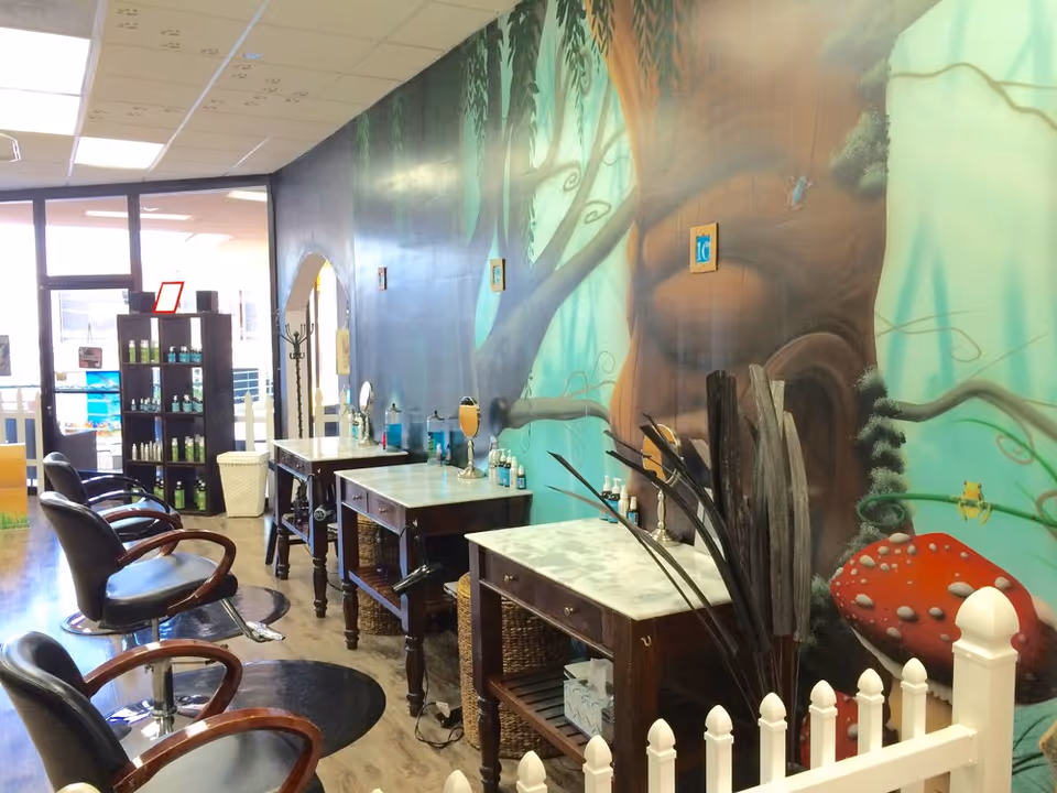 Salon chairs and styling stations line a mural-covered interior with hair products displayed.