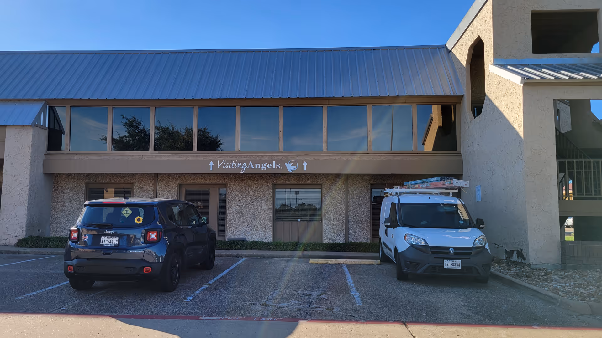 Facade of Visiting Angels Senior Home Care building with two parked vehicles in front.