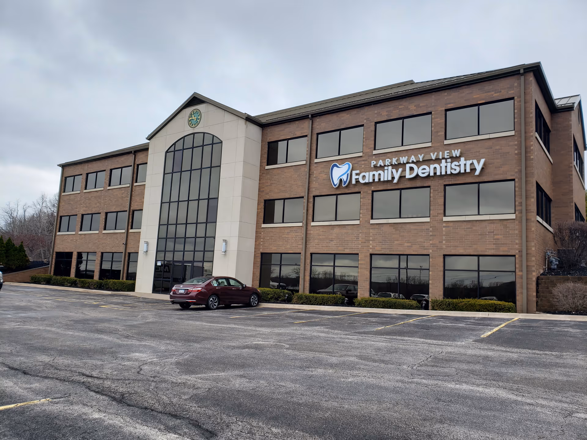 Brick office-style building with a tall central glass entrance and a parking lot.