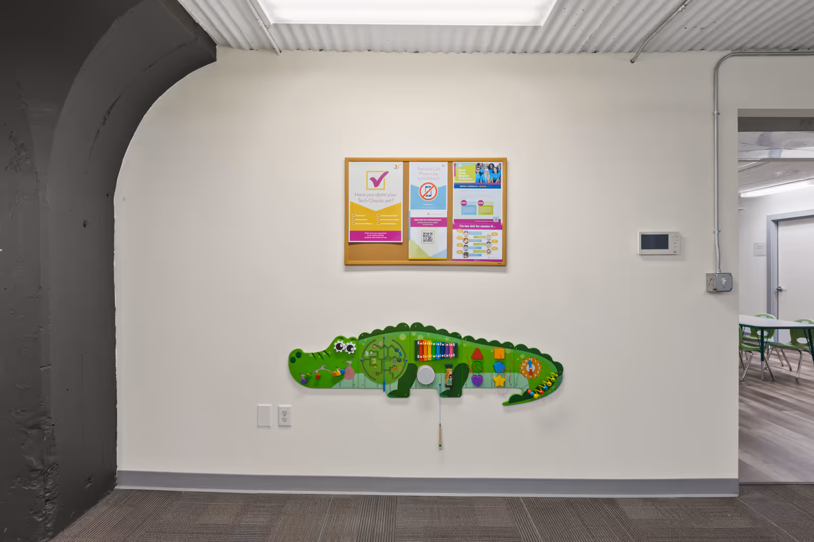 White wall with a colorful bulletin board and a green alligator wall decoration in a hallway.