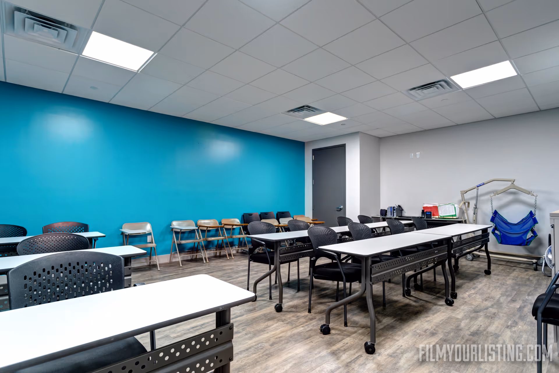 Bright multipurpose room in Ultimate Care NY with long white tables and teal wall.