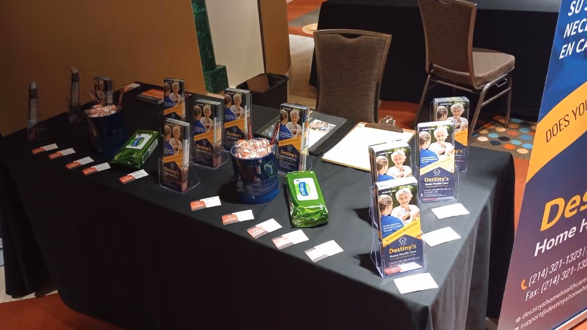 Table with Destiny's Home Health Care brochures and displays in an indoor conference area.