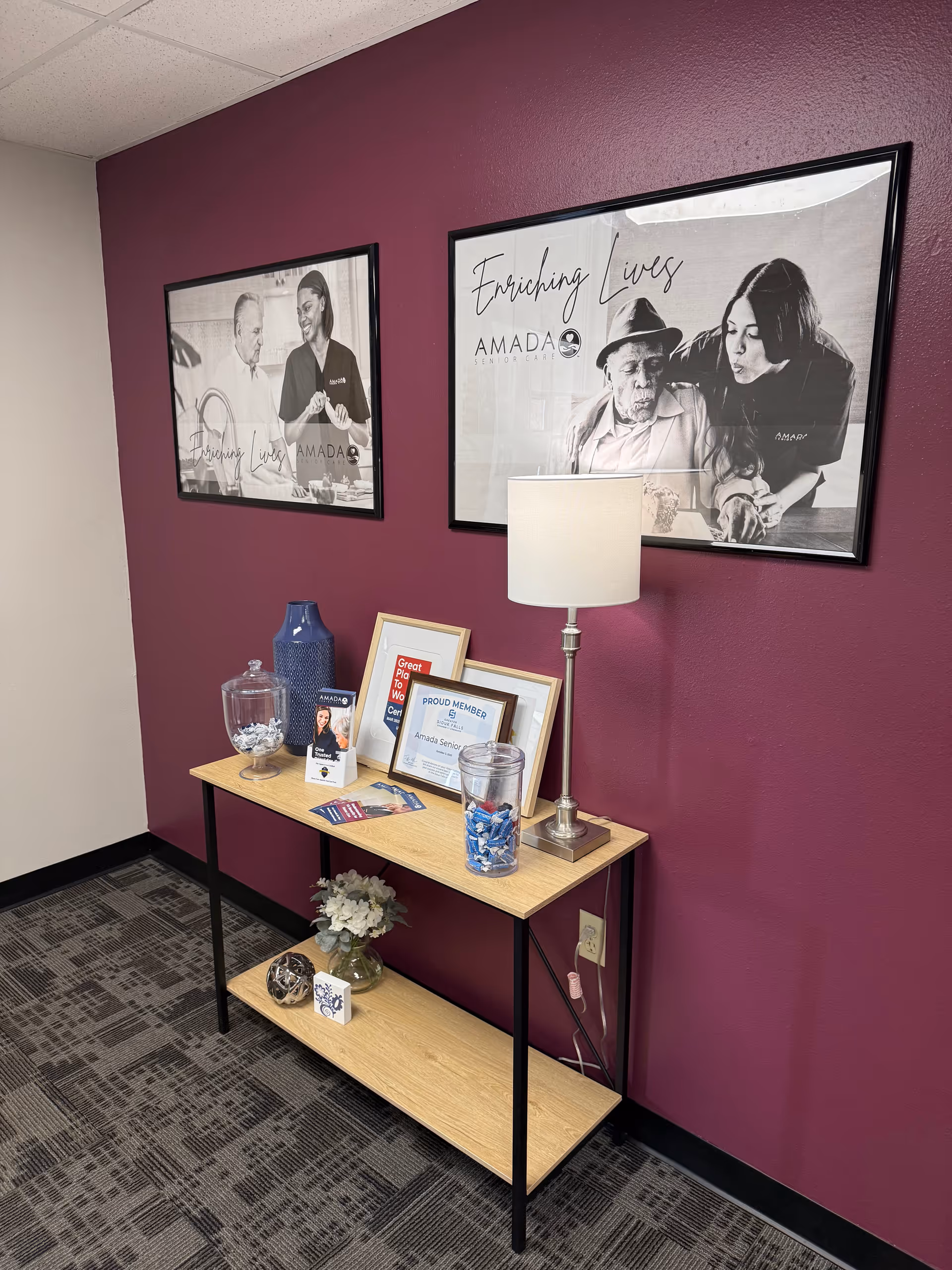 A console table with framed posters, a lamp, and decor against a purple wall.