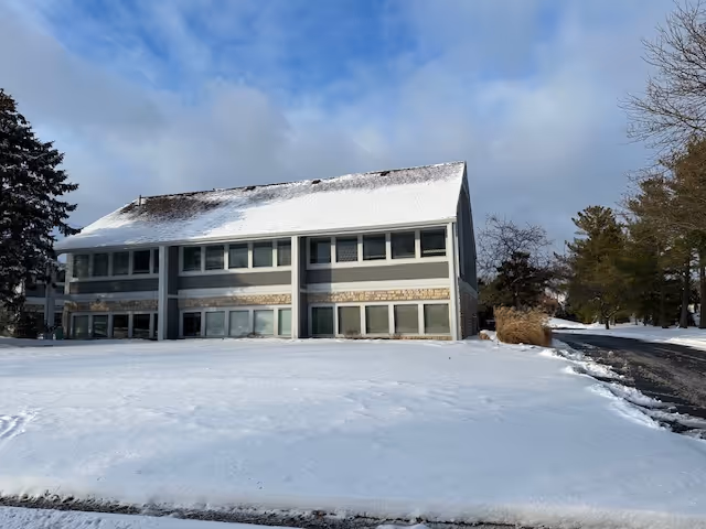 Two-story facility building with a snow-covered lawn and a road in front.