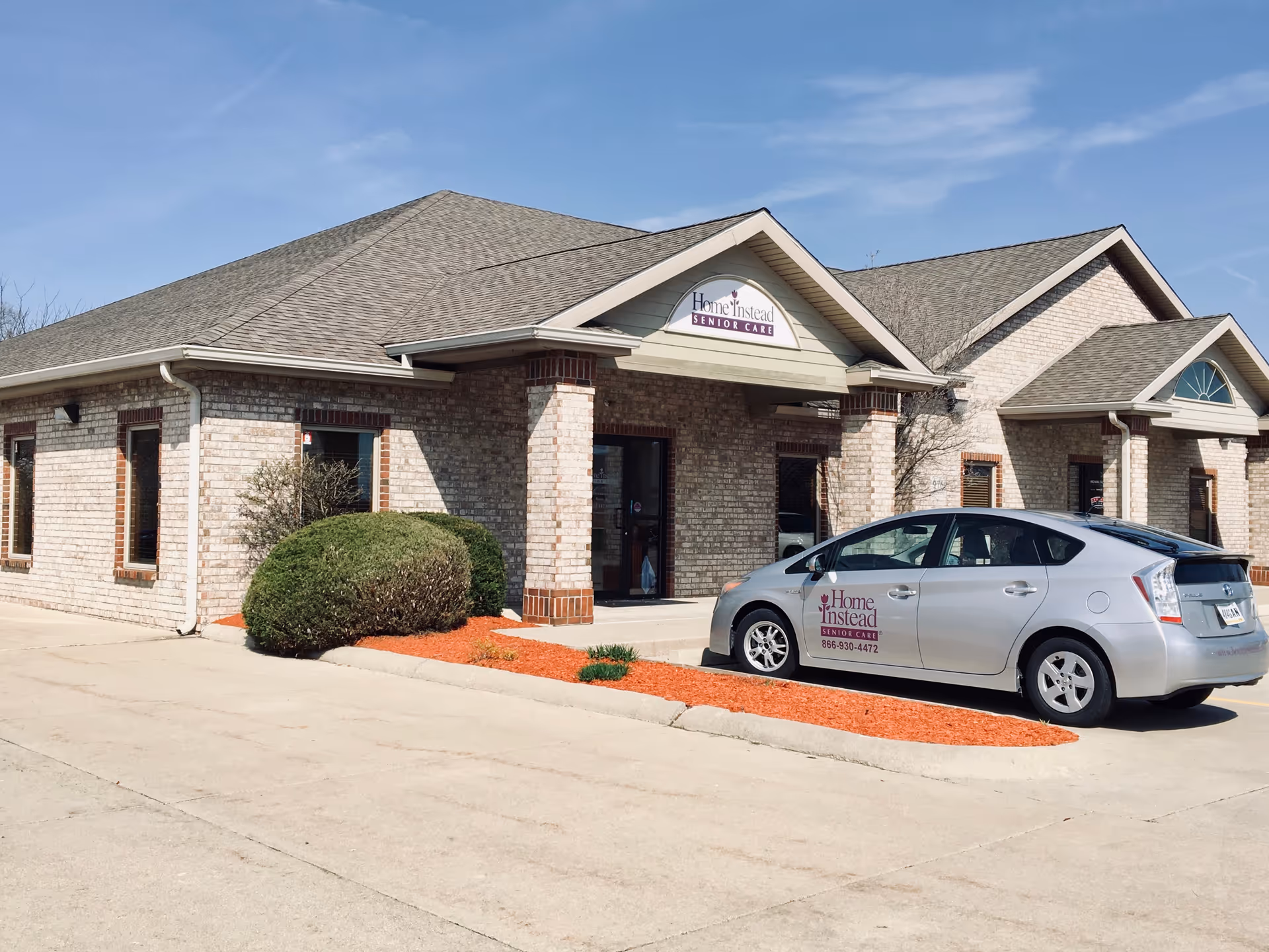 Front view of a brick senior care facility with a parked Home Instead car.