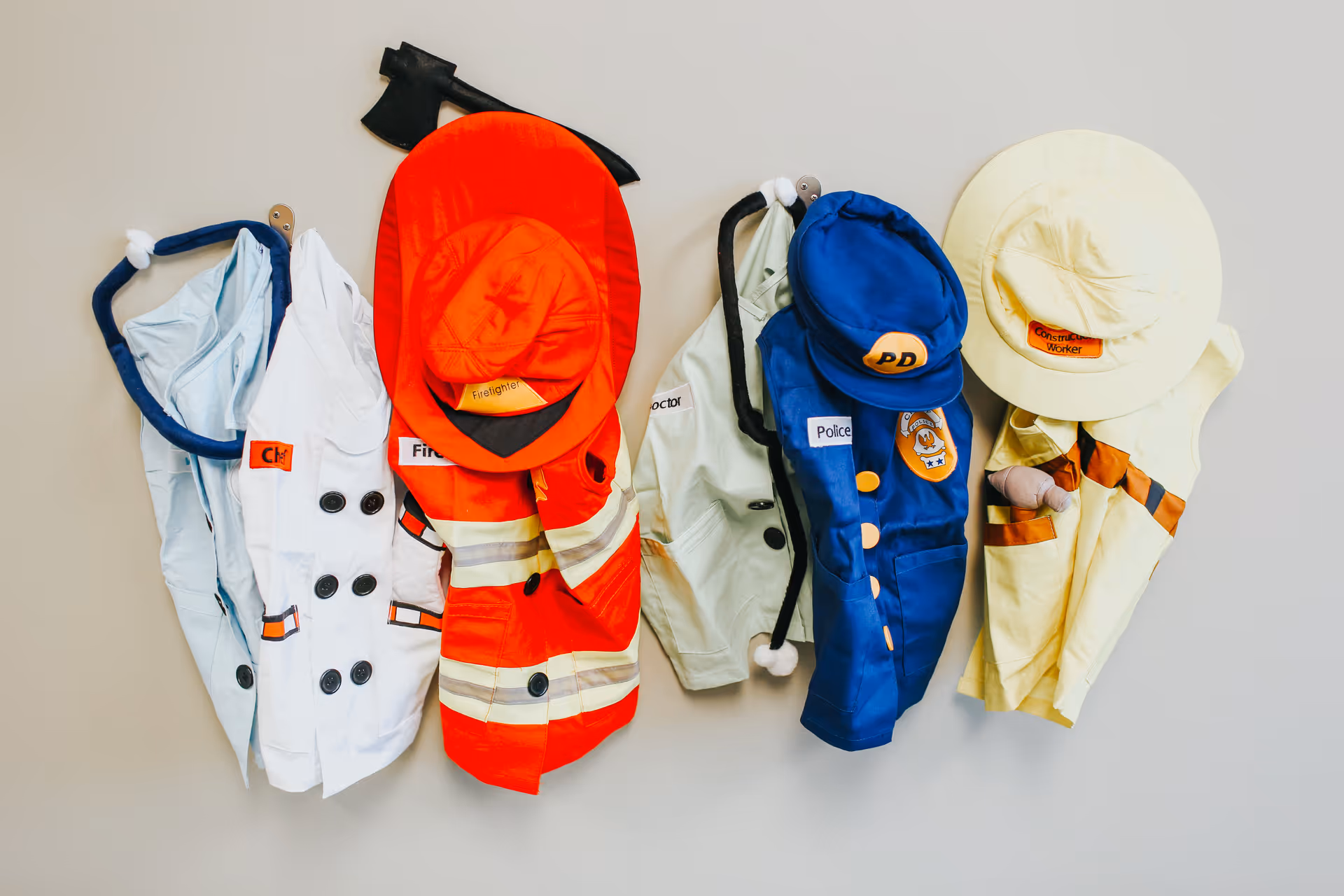 Row of colorful firefighter, police, and other costumes hanging on a wall.