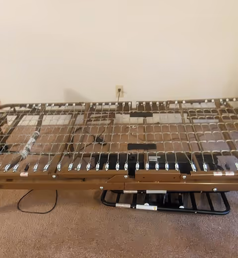Metal hospital-style bed frame with slats sits in a bare beige room.