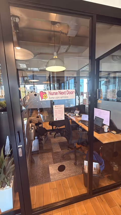 Glass-walled reception area with desks, computers, and a Nurse Next Door sign