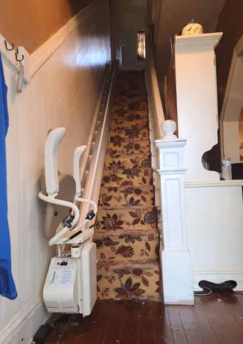 Interior staircase featuring a wall-mounted stairlift chair along a floral carpet.
