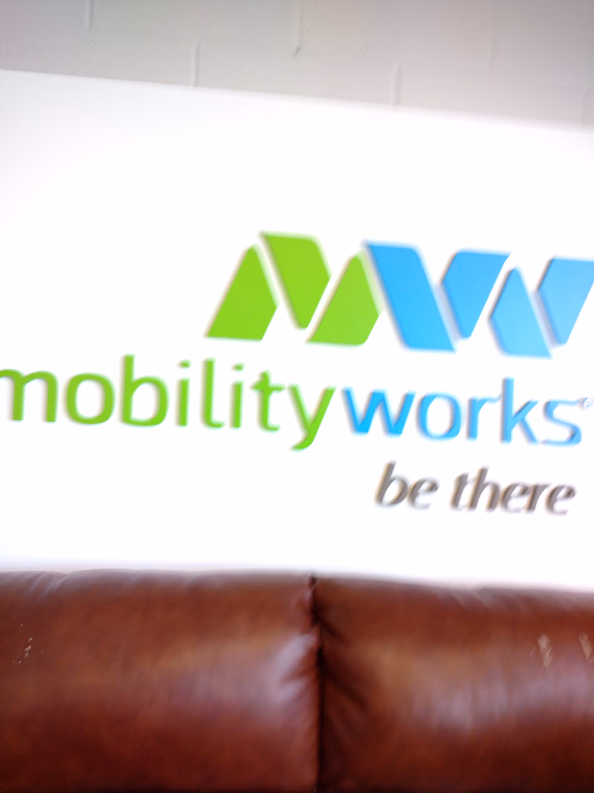 Interior lounge area with MobilityWorks logo on wall and brown leather couch