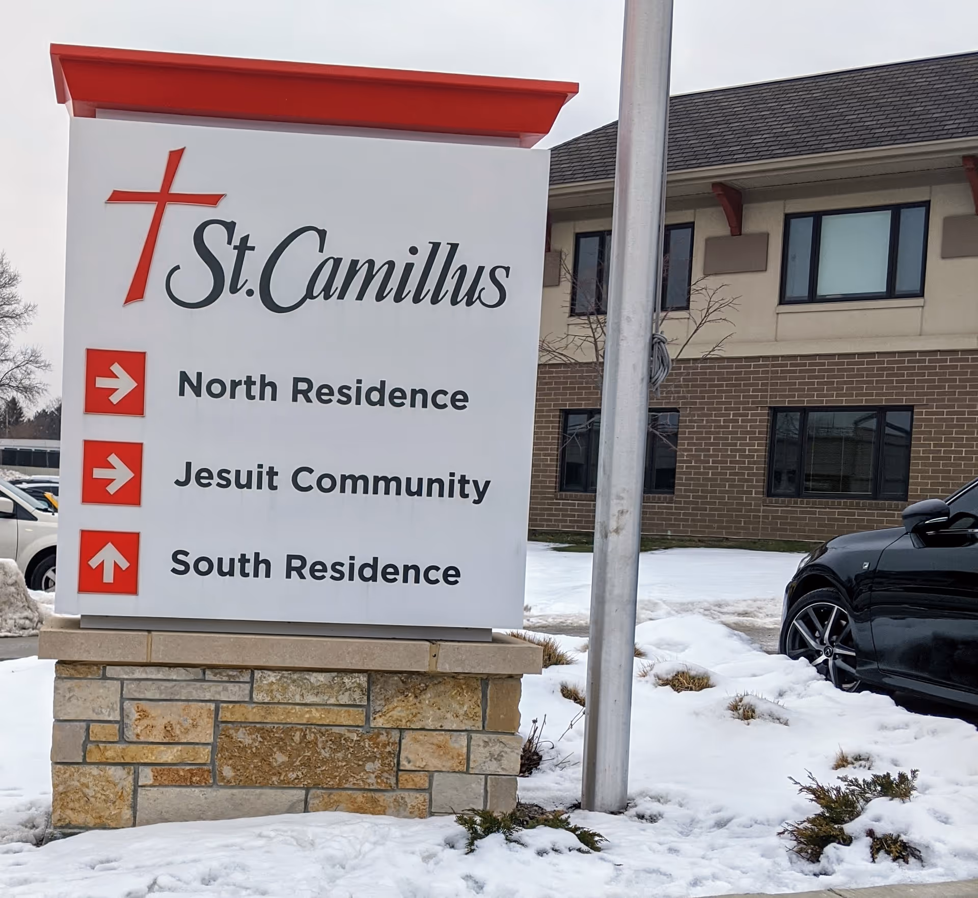 Outdoor sign for St. Camillus with arrows to North, Jesuit, and South Residences near a building