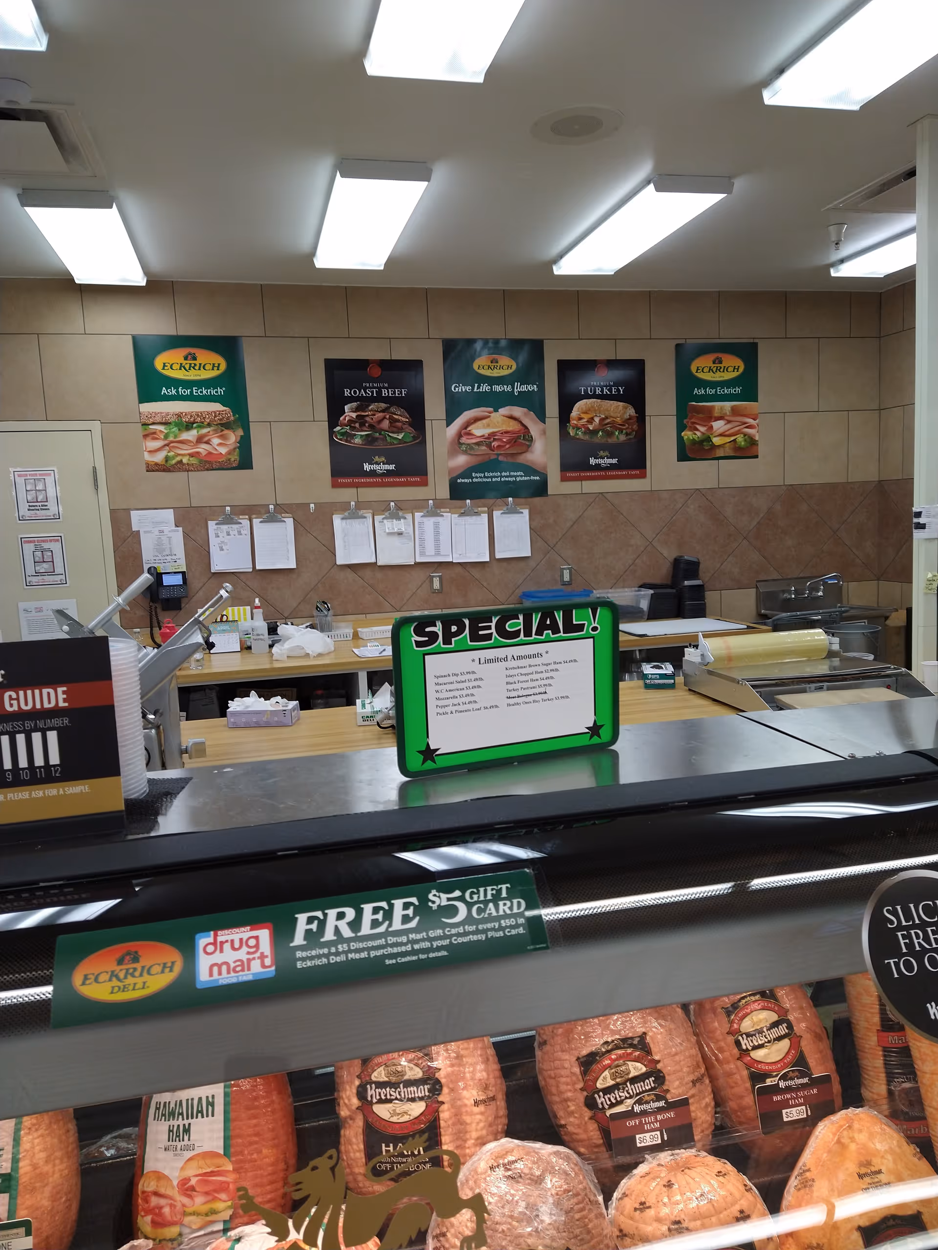 Interior of a Discount Drug Mart deli counter with meats, signs, and posters.