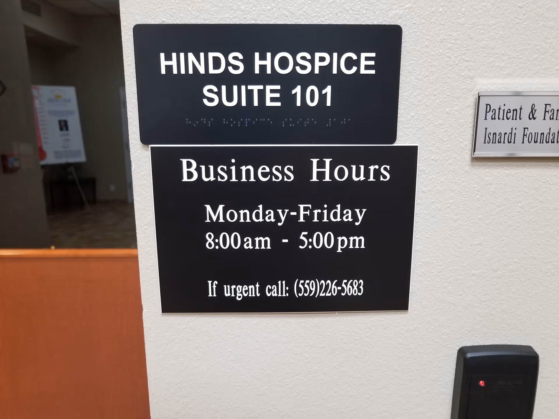 Wall-mounted signs display Hinds Hospice Suite 101 and business hours inside a hallway.