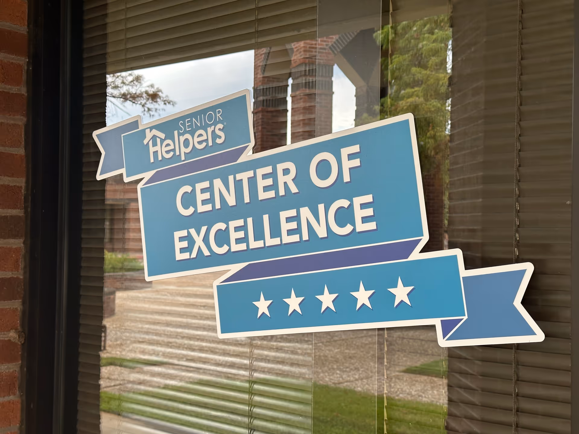 Blue Center of Excellence sign with Senior Helpers logo on a window.