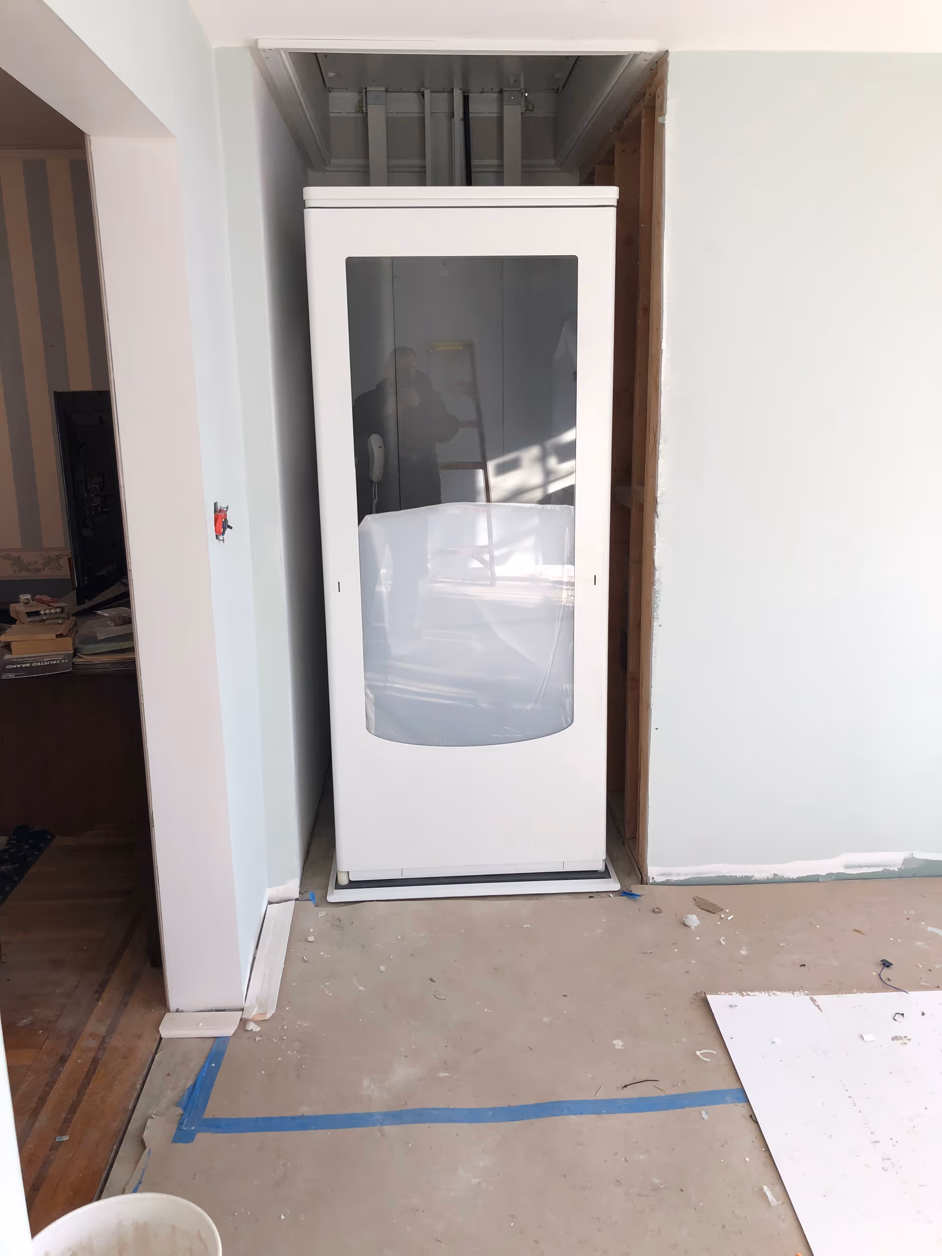 Unfinished interior with a tall white shower enclosure in a doorway, construction debris on the floor.