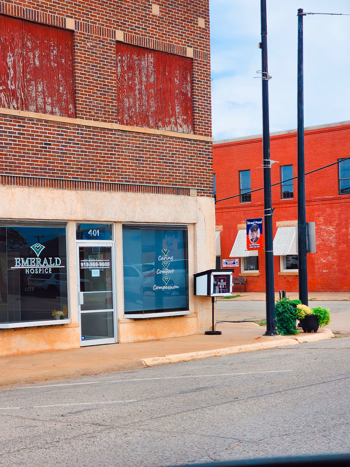 Brick storefront displaying Emerald Hospice signage along a sidewalk.