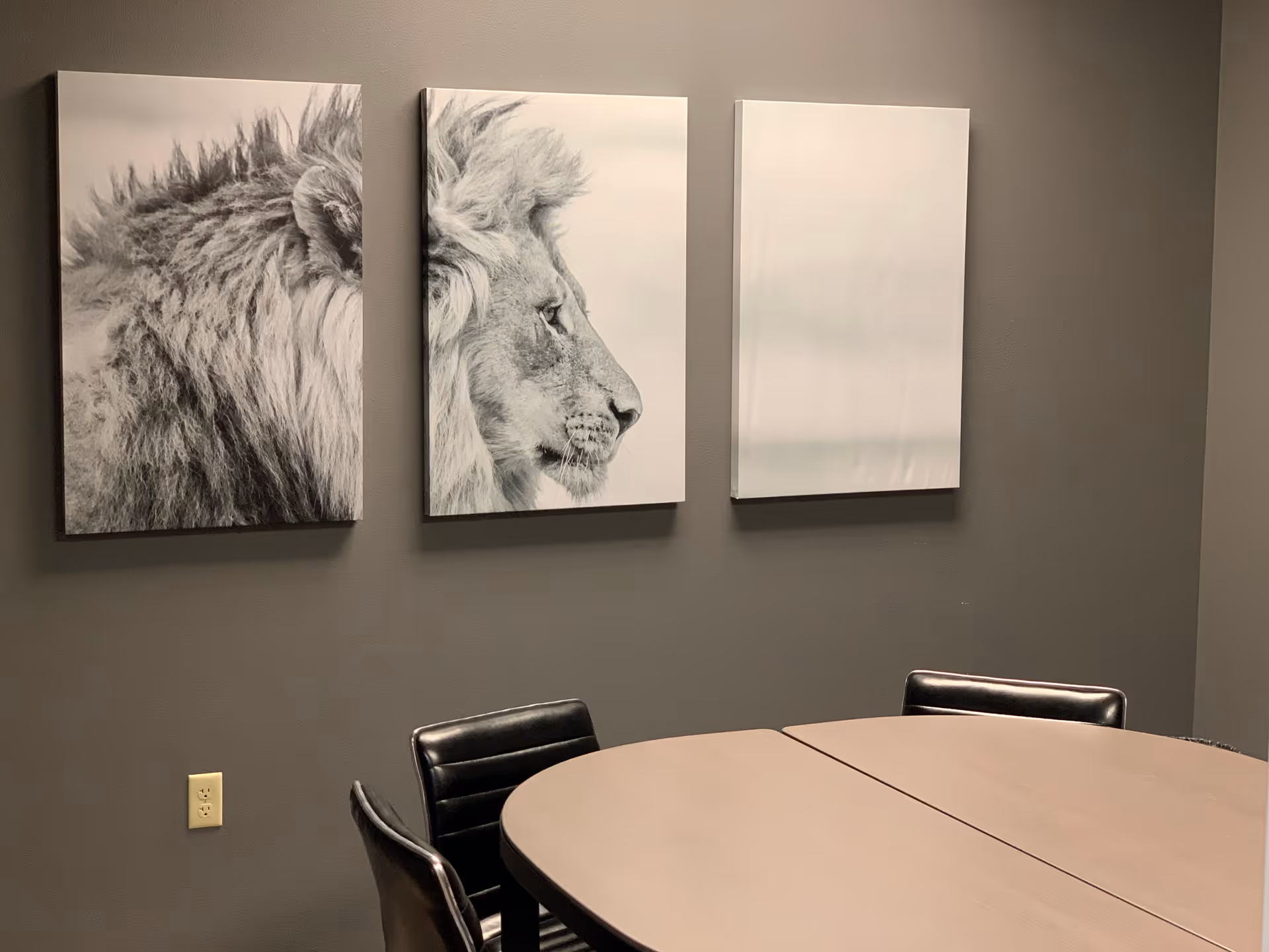 Gray-walled room with round table, black chairs, and three lion art prints.