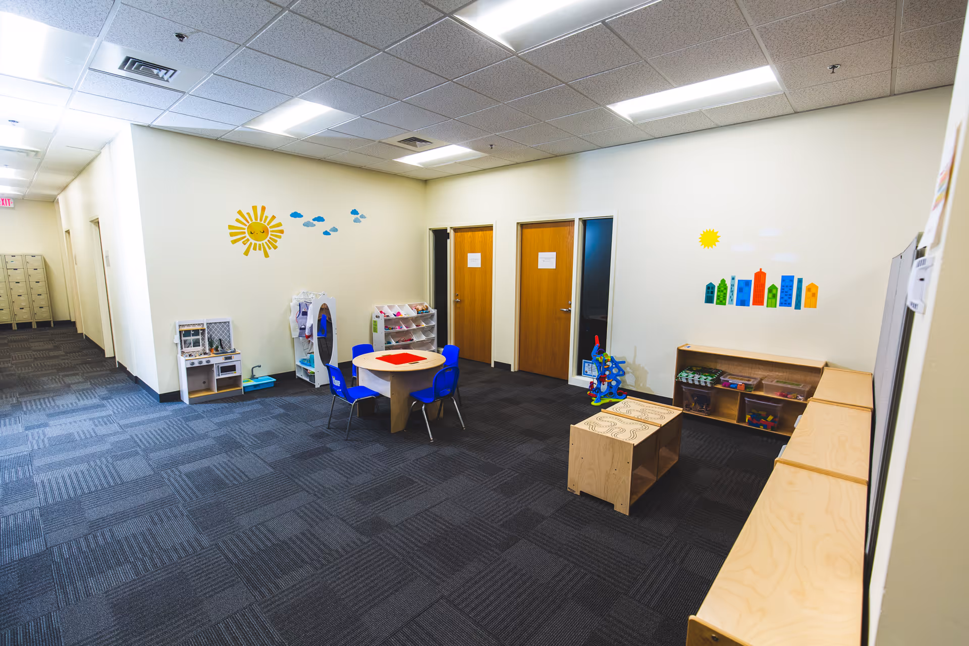 Interior playroom in a senior living facility with a round table, blue chairs, and toys.