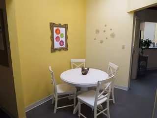 Round white table with four white chairs in a yellow-walled dining area.