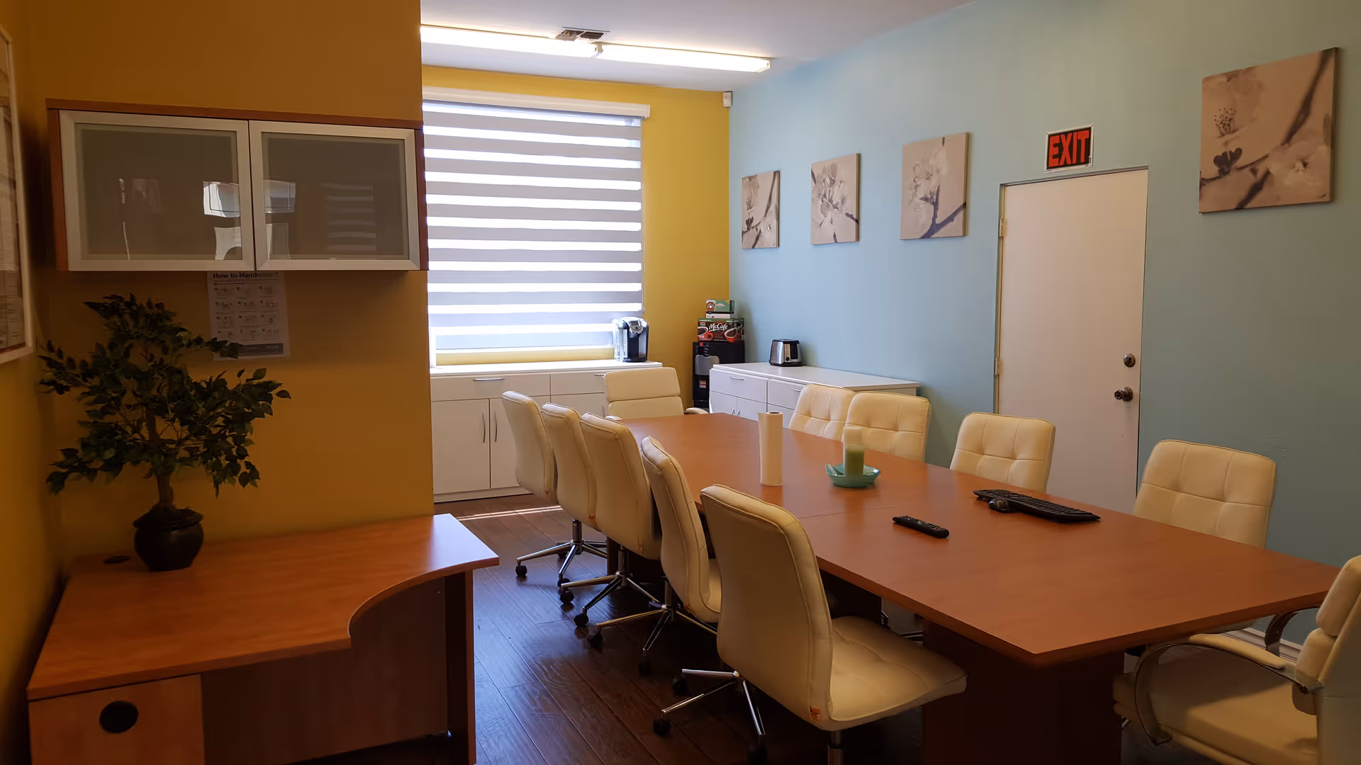 A long wooden conference table surrounded by white chairs in a bright dining room.