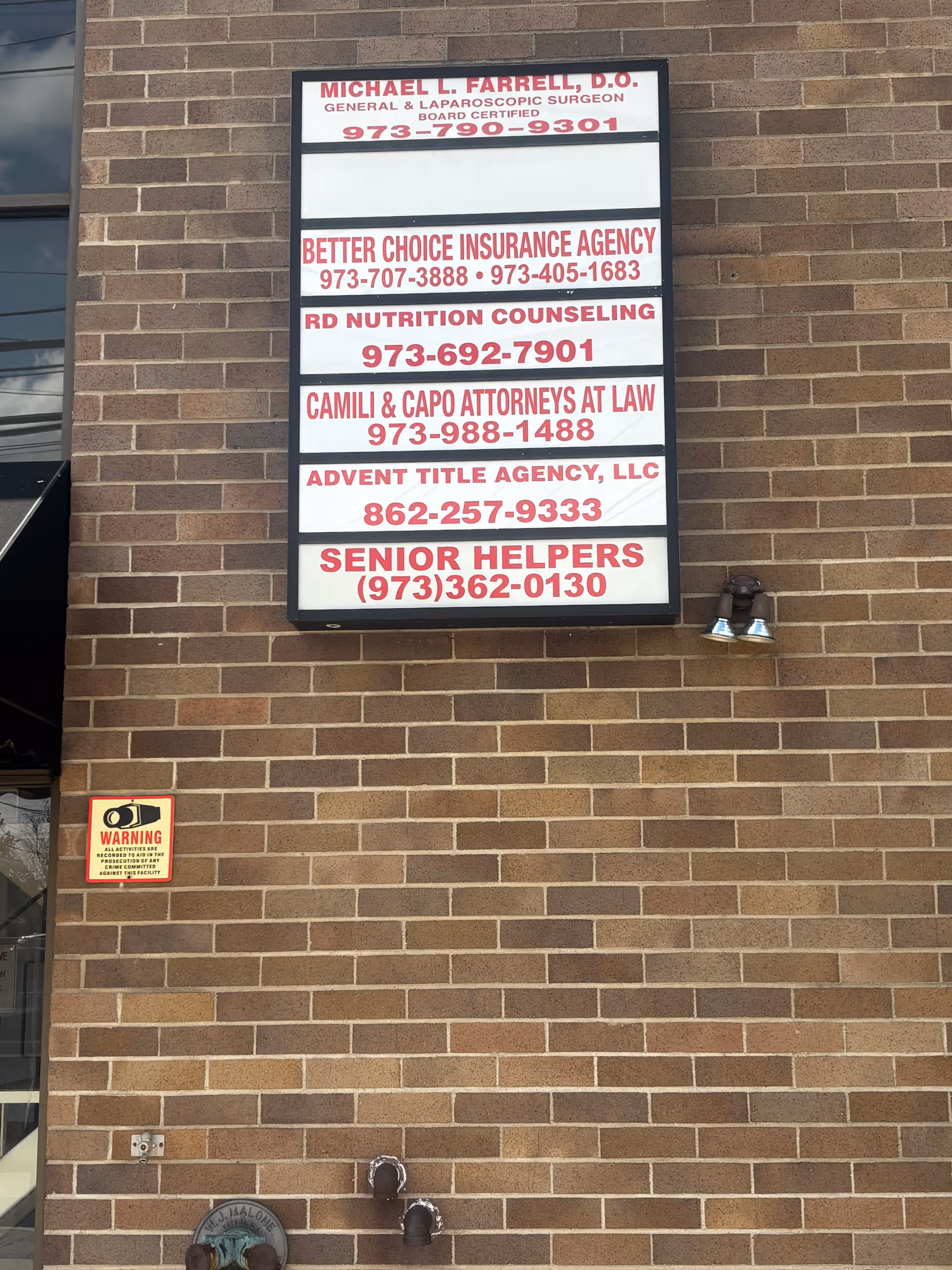 Exterior brick wall with a multi-tenant signboard listing businesses and Senior Helpers contact info.