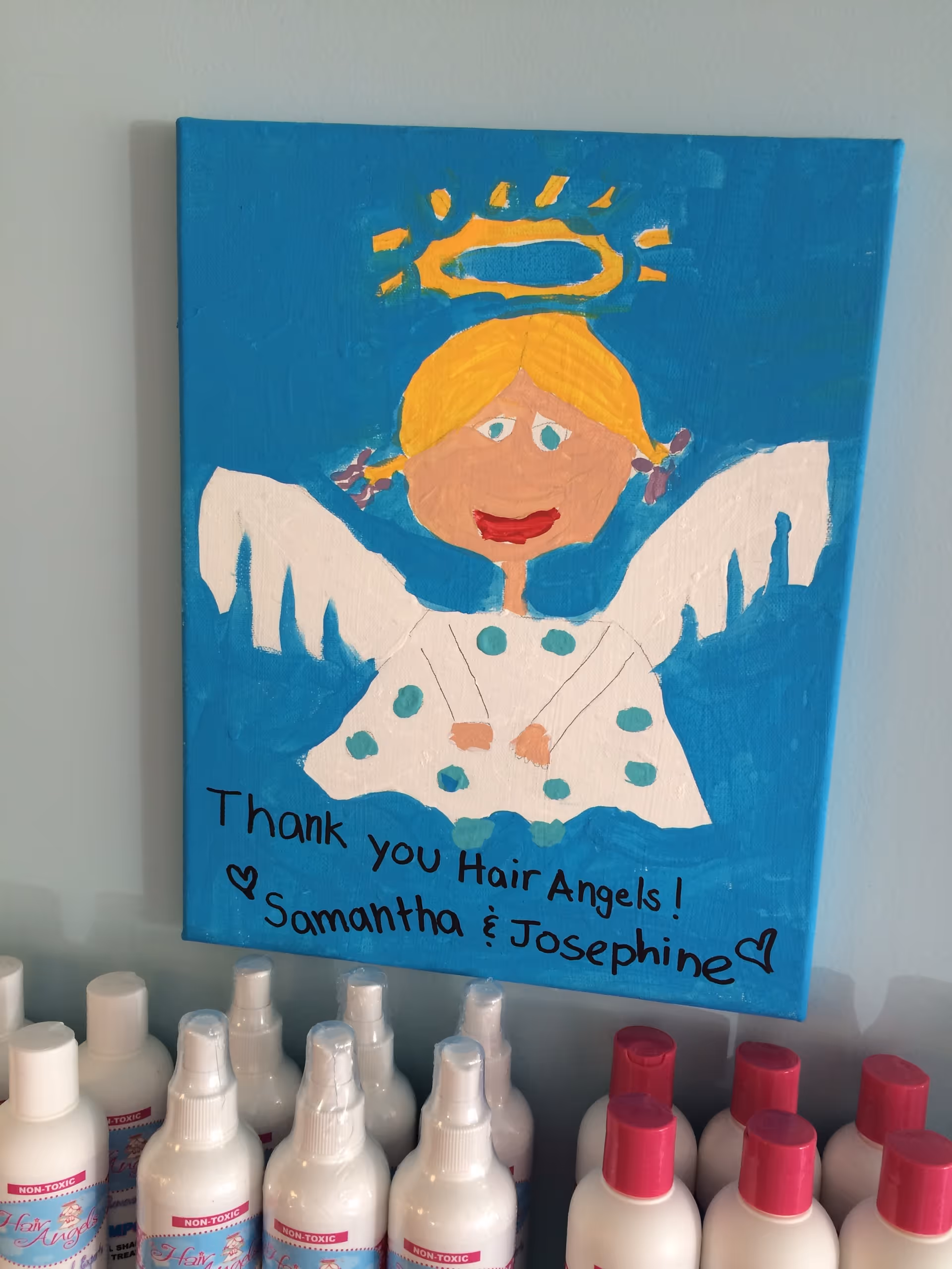 Bright blue painting of an angel reads 'Thank you Hair Angels' with hair product bottles below.