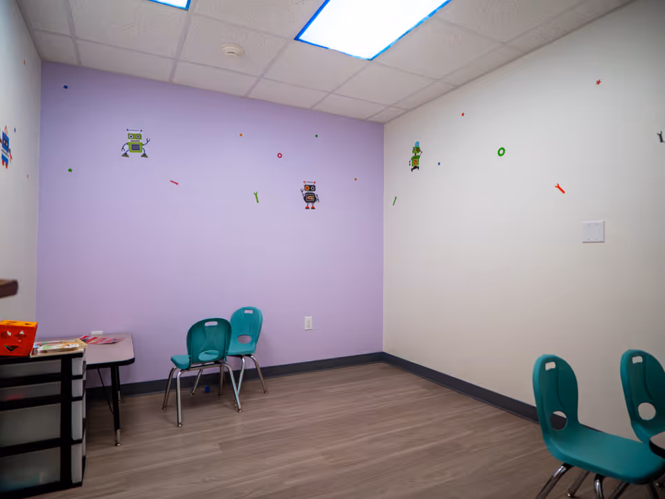 Small child-friendly therapy room with purple wall, teal chairs, and robot decals.