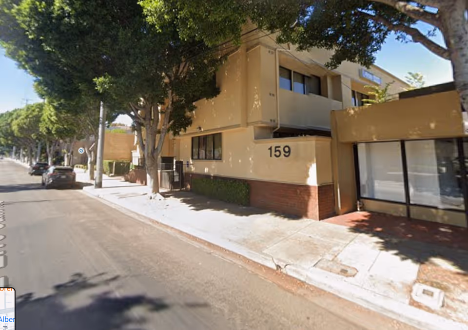 Two-story beige building with street number 159 along a tree-lined sidewalk.
