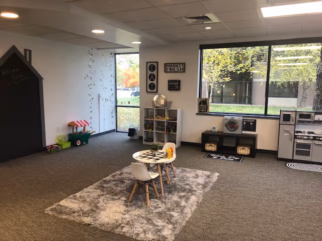 A small table with chairs sits on a shaggy rug in a bright activity room.