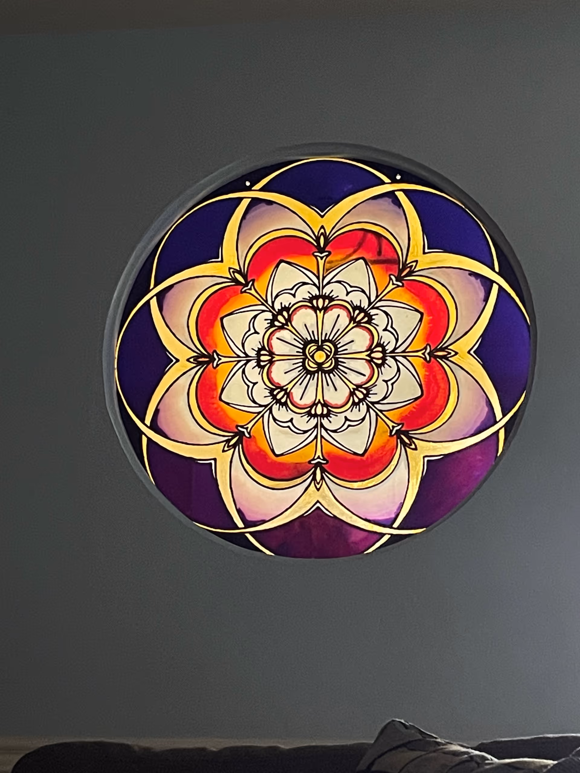 Circular stained glass style light fixture on a gray wall in a living area.