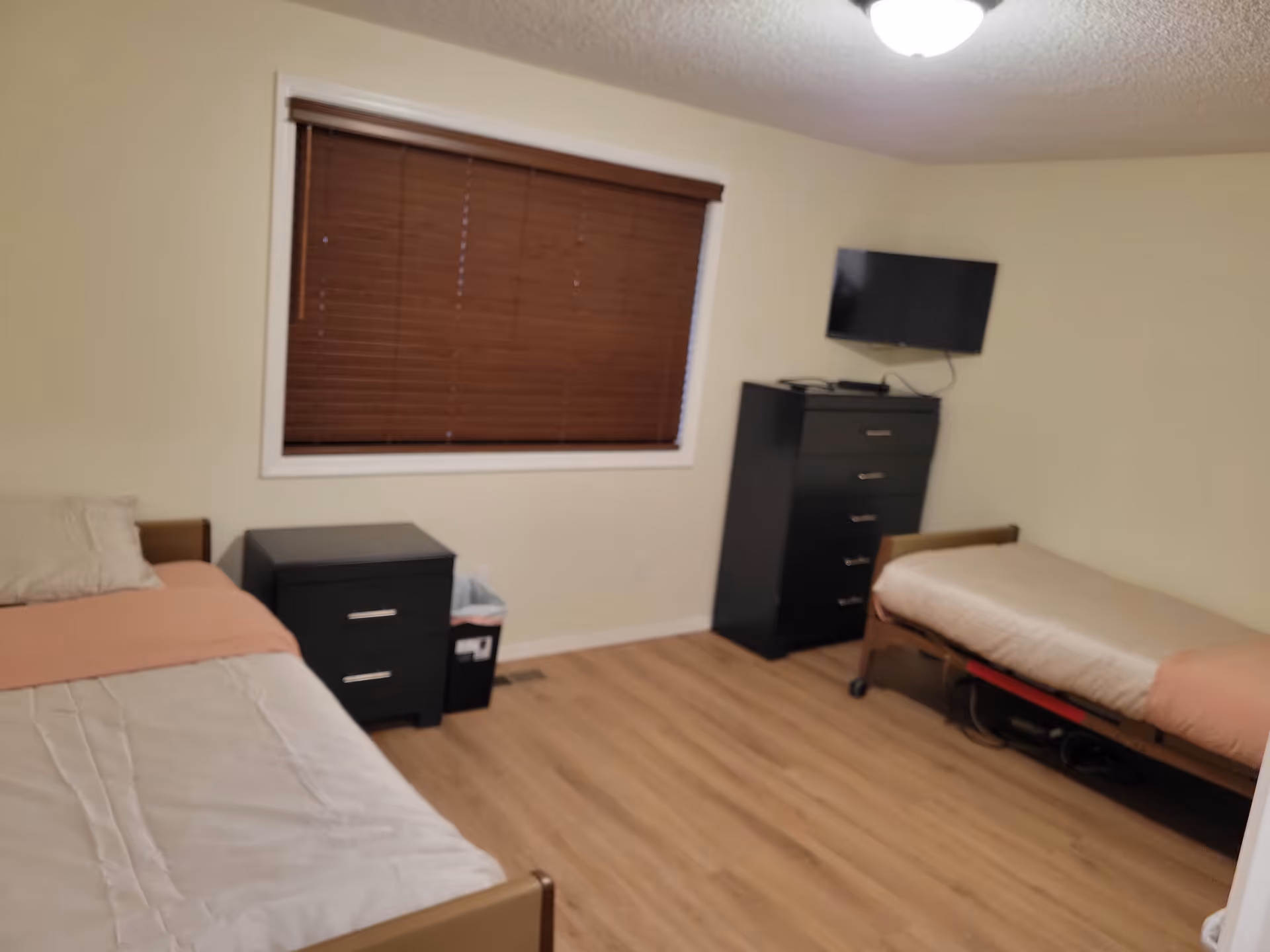Two single beds with a nightstand and tall dresser in a small beige bedroom.