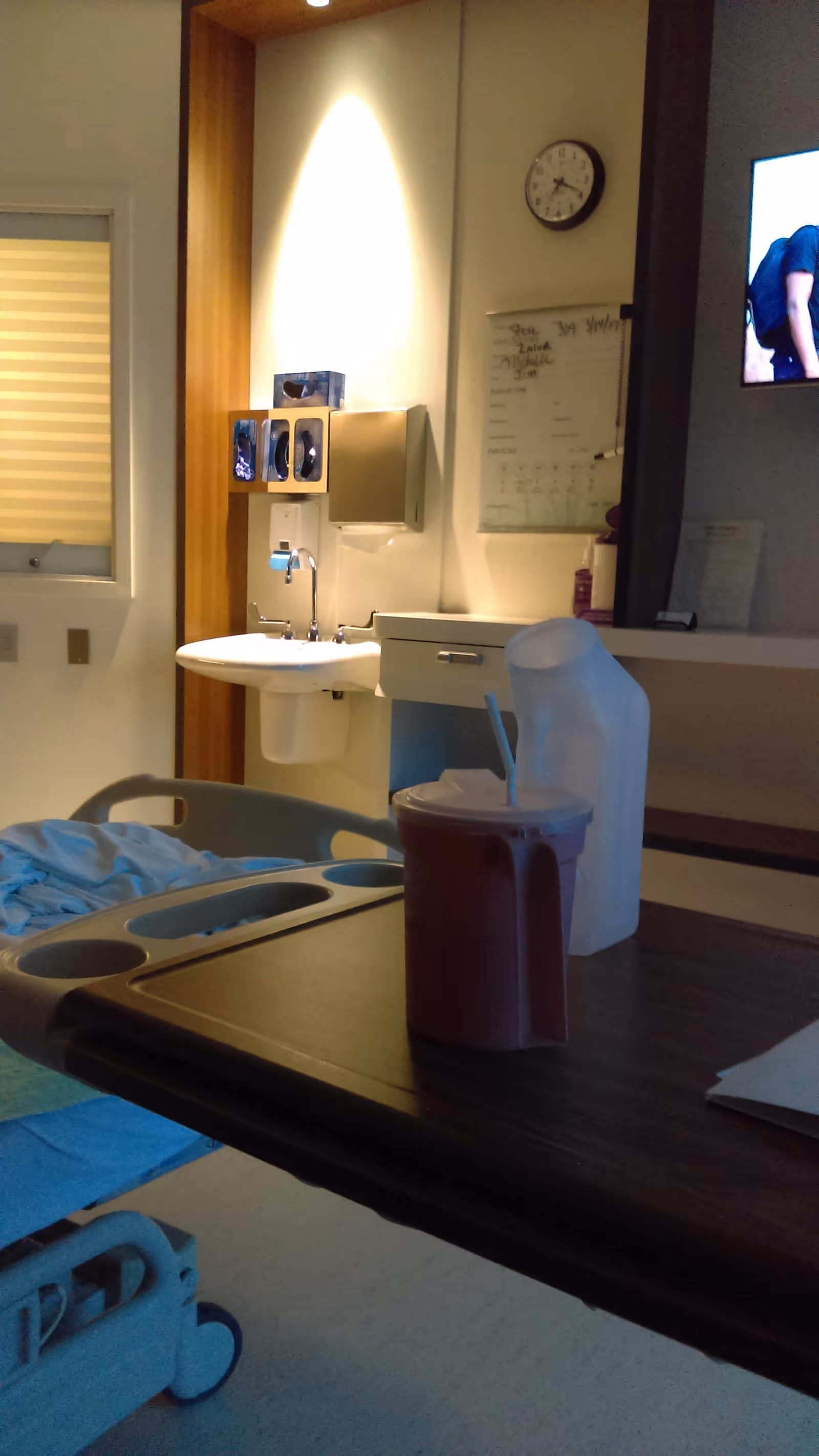 Interior hospital room with a bed, sink, wall clock, and a beverage pitcher on a table.