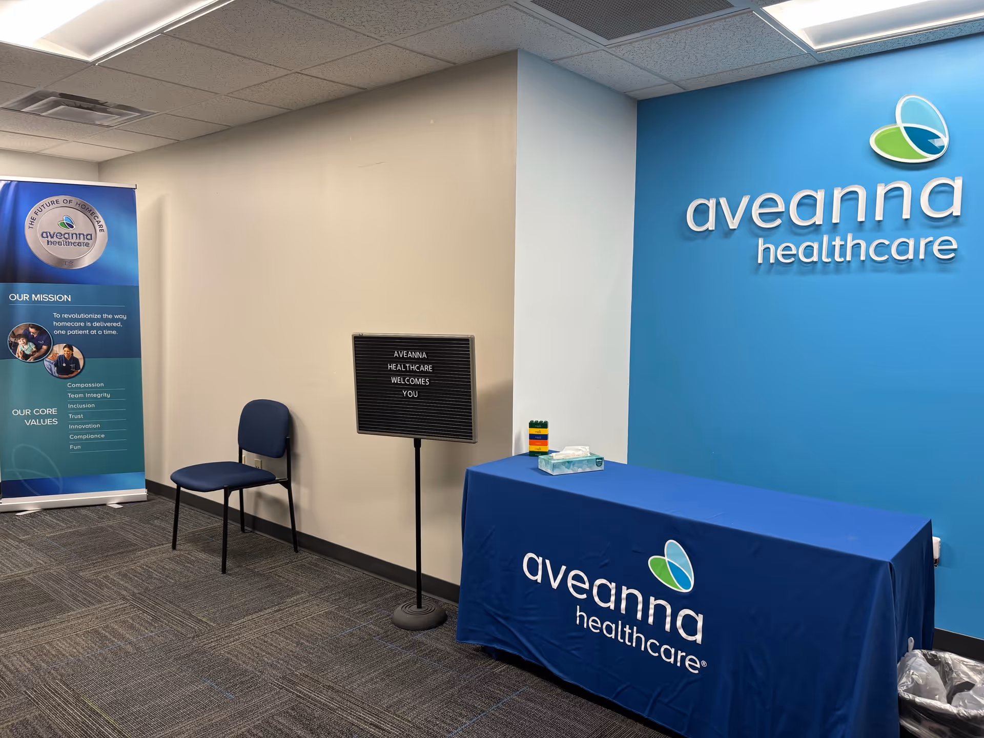 Interior reception area with Aveanna Healthcare branding, banner, and blue tablecloth.