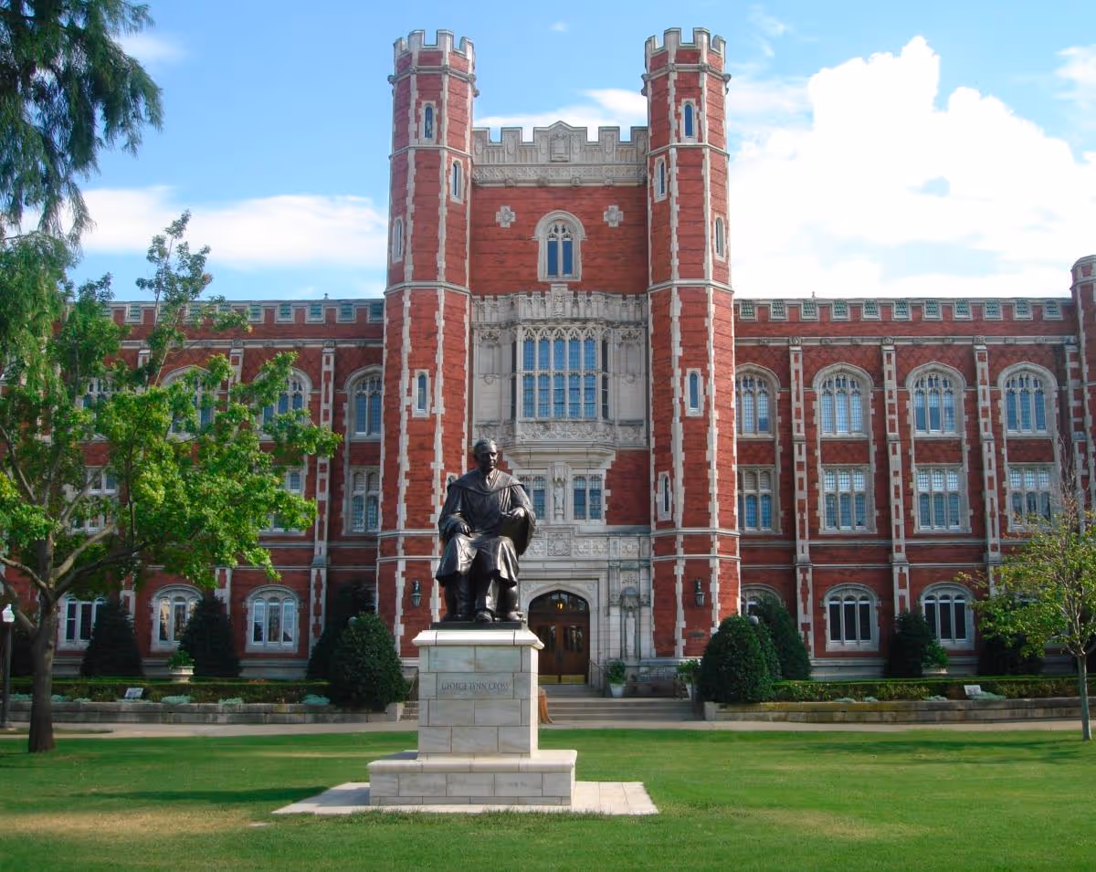 Red brick building with twin towers and a statue on a manicured front lawn.