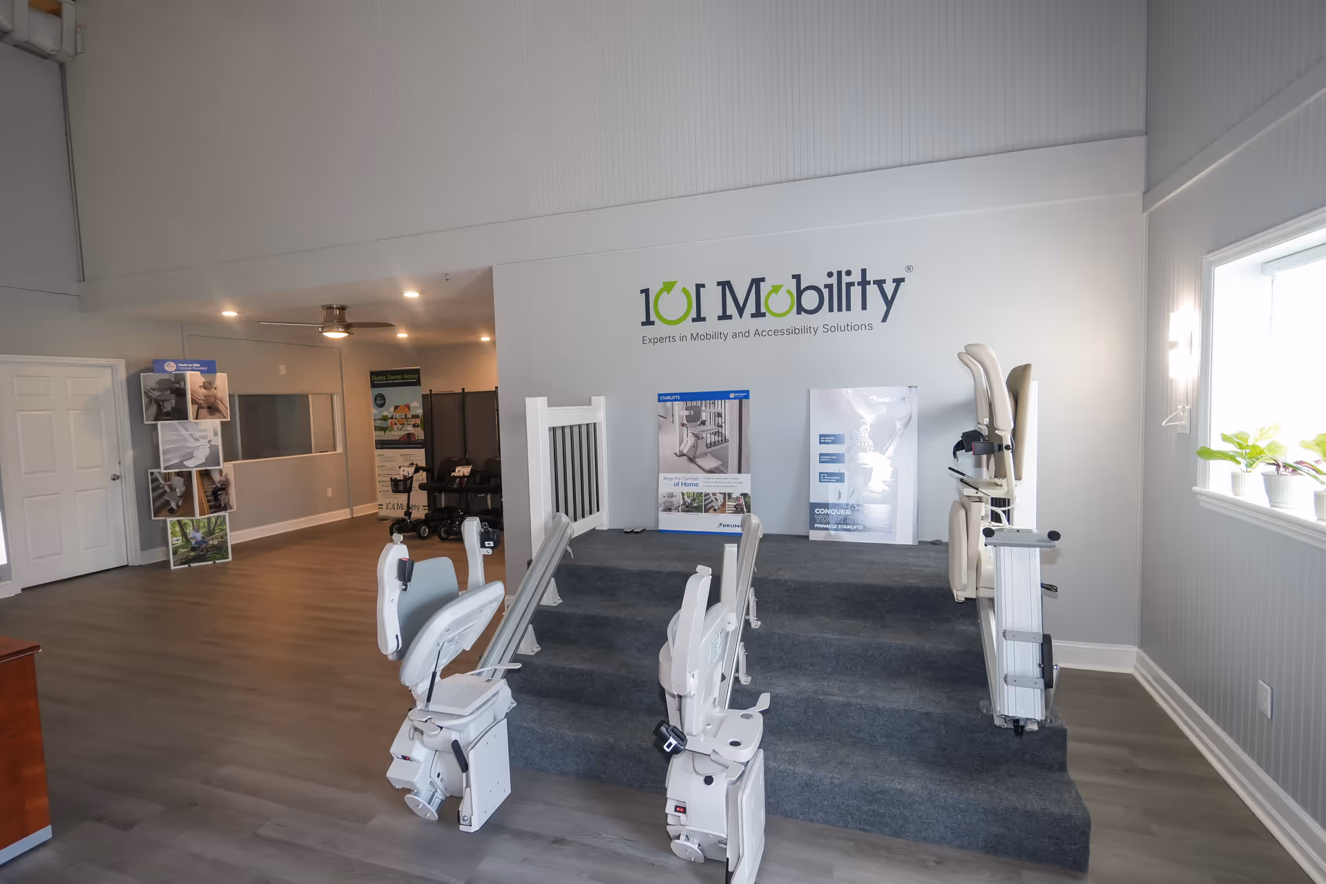 Interior showroom with stairlifts and mobility equipment beside a logo wall.