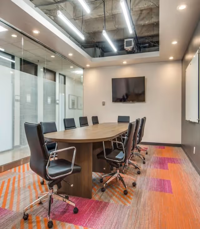 A modern conference room with a long wooden table and glass walls.