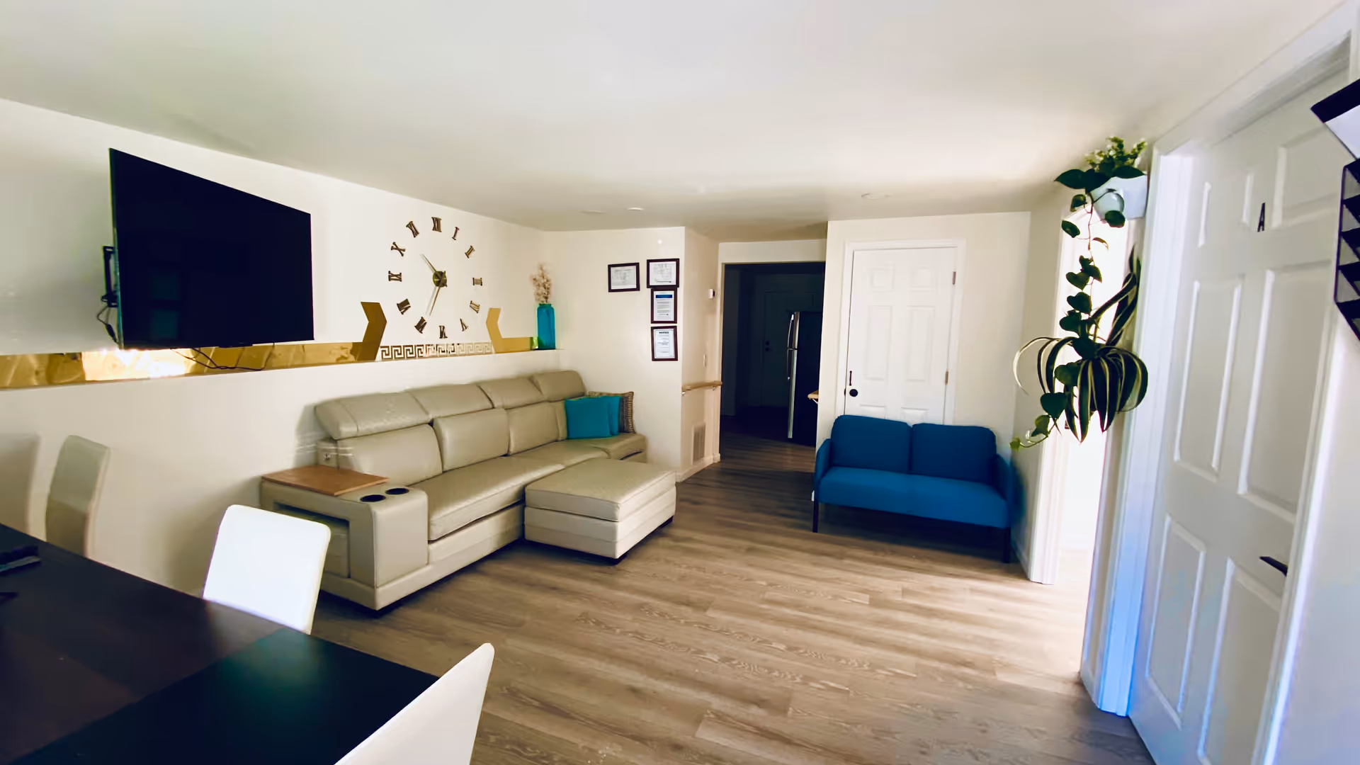 Modern living room with beige sectional sofa, blue armchair, mounted TV, and potted plants.