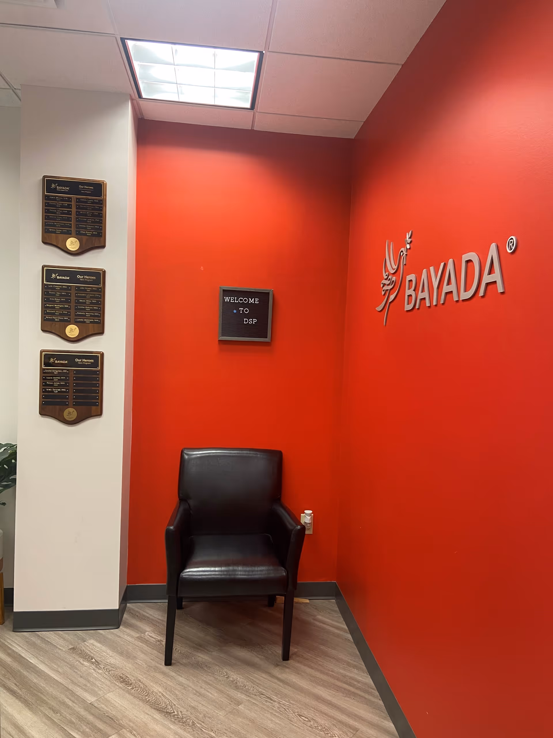 Red-walled lobby with BAYADA logo, a black chair, and wall plaques.