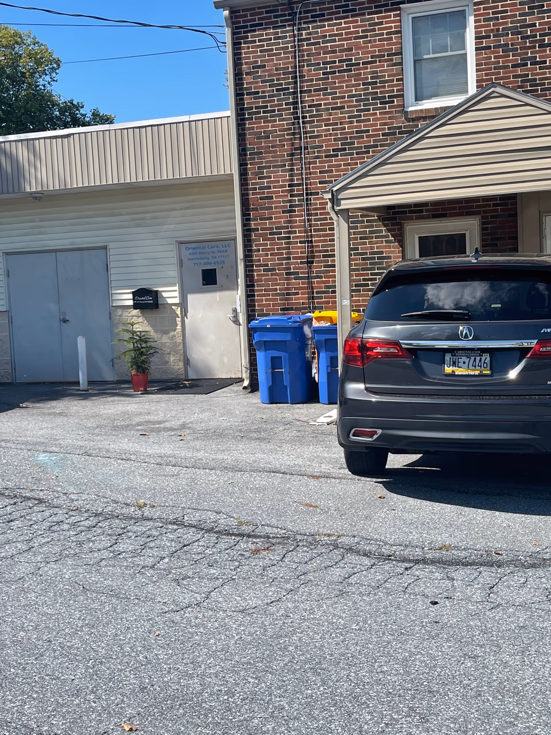 Exterior view of Oriental Care LLC entrance with blue bins and a parked SUV.