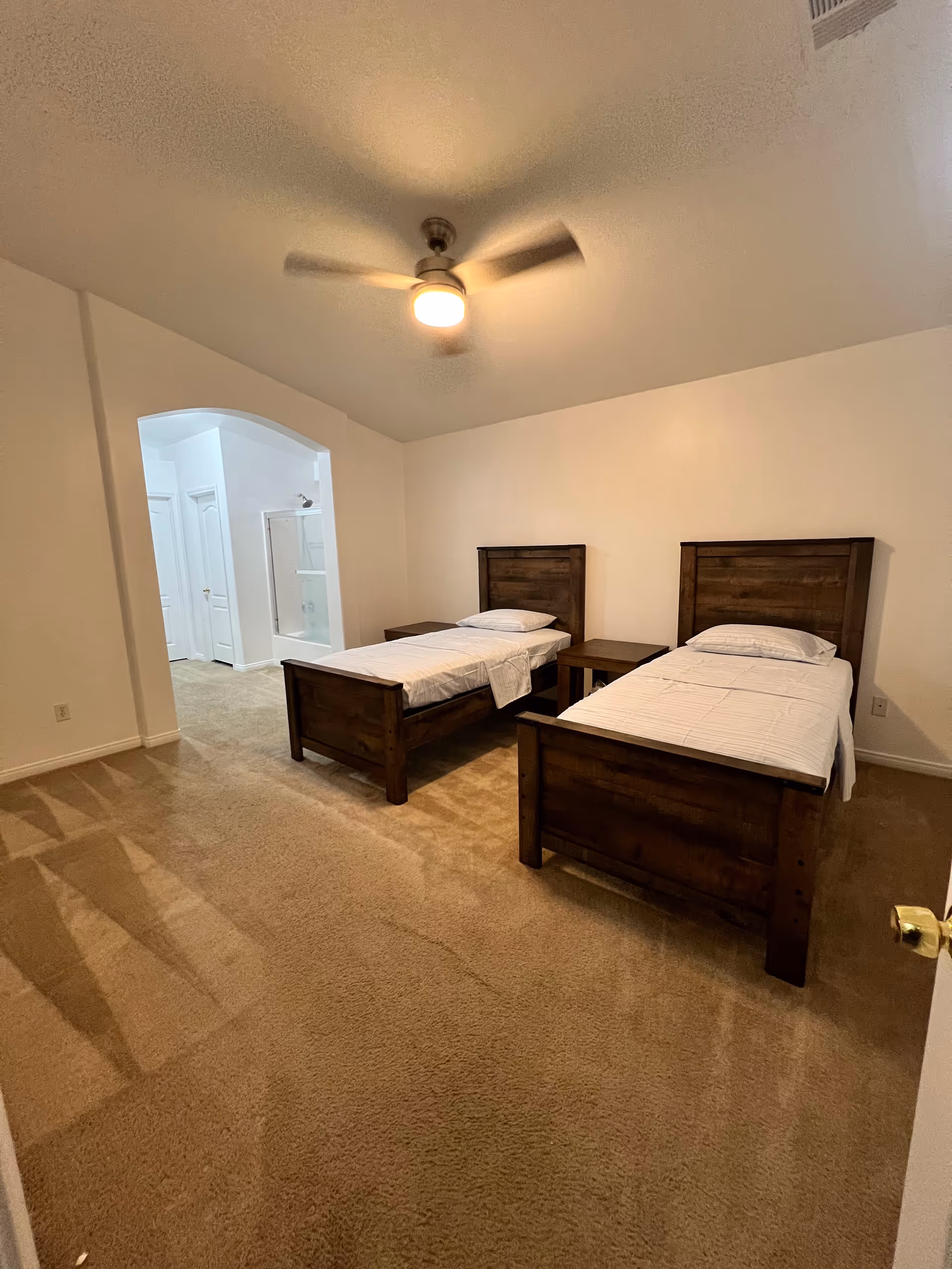 Two wooden twin beds with nightstands in a beige carpeted bedroom.