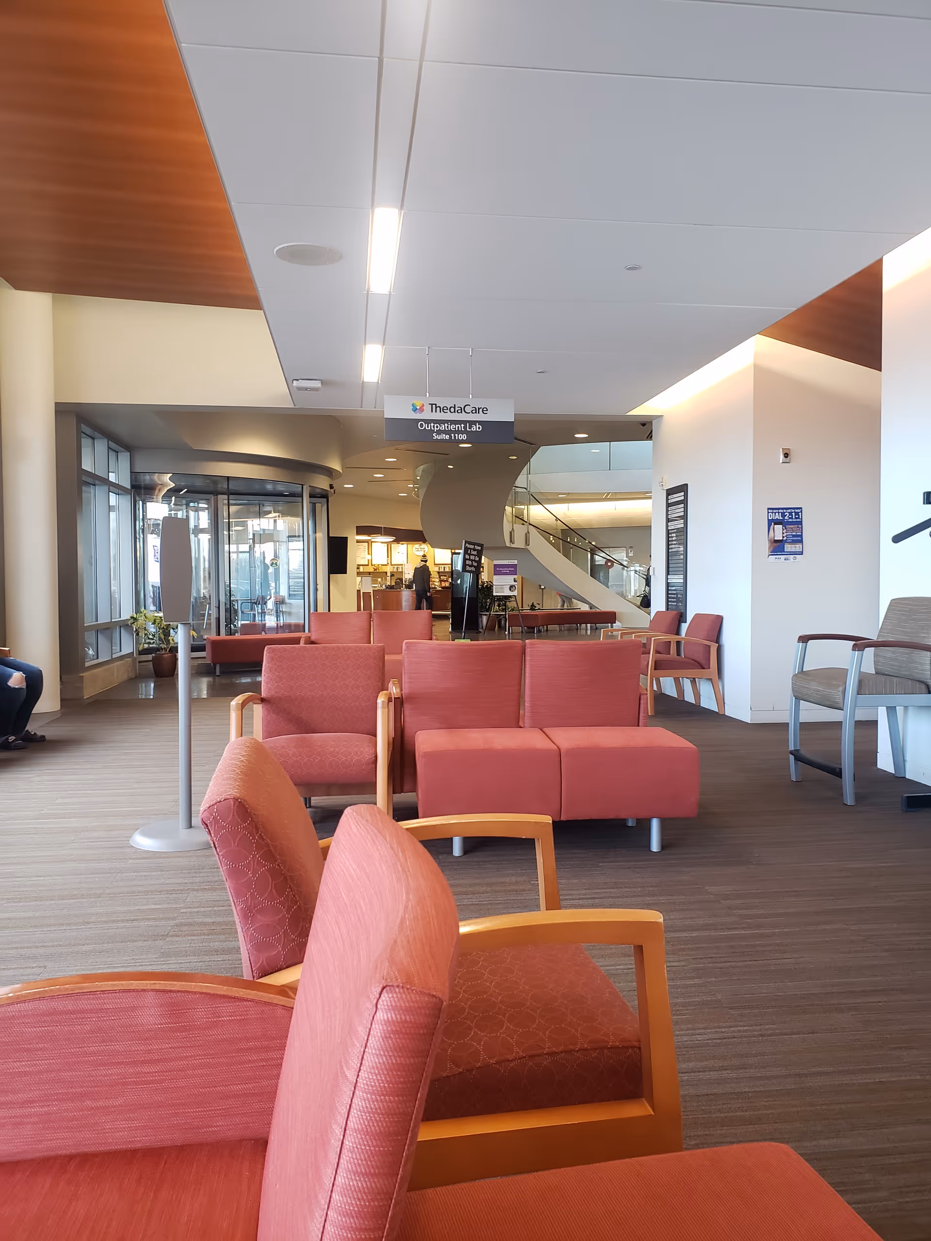 Modern medical facility lobby with red seating and a curved staircase