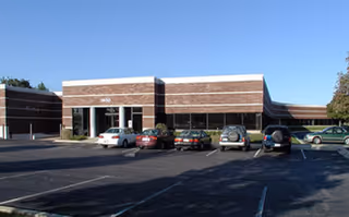Front view of a brick building with a parking lot and several cars outside.