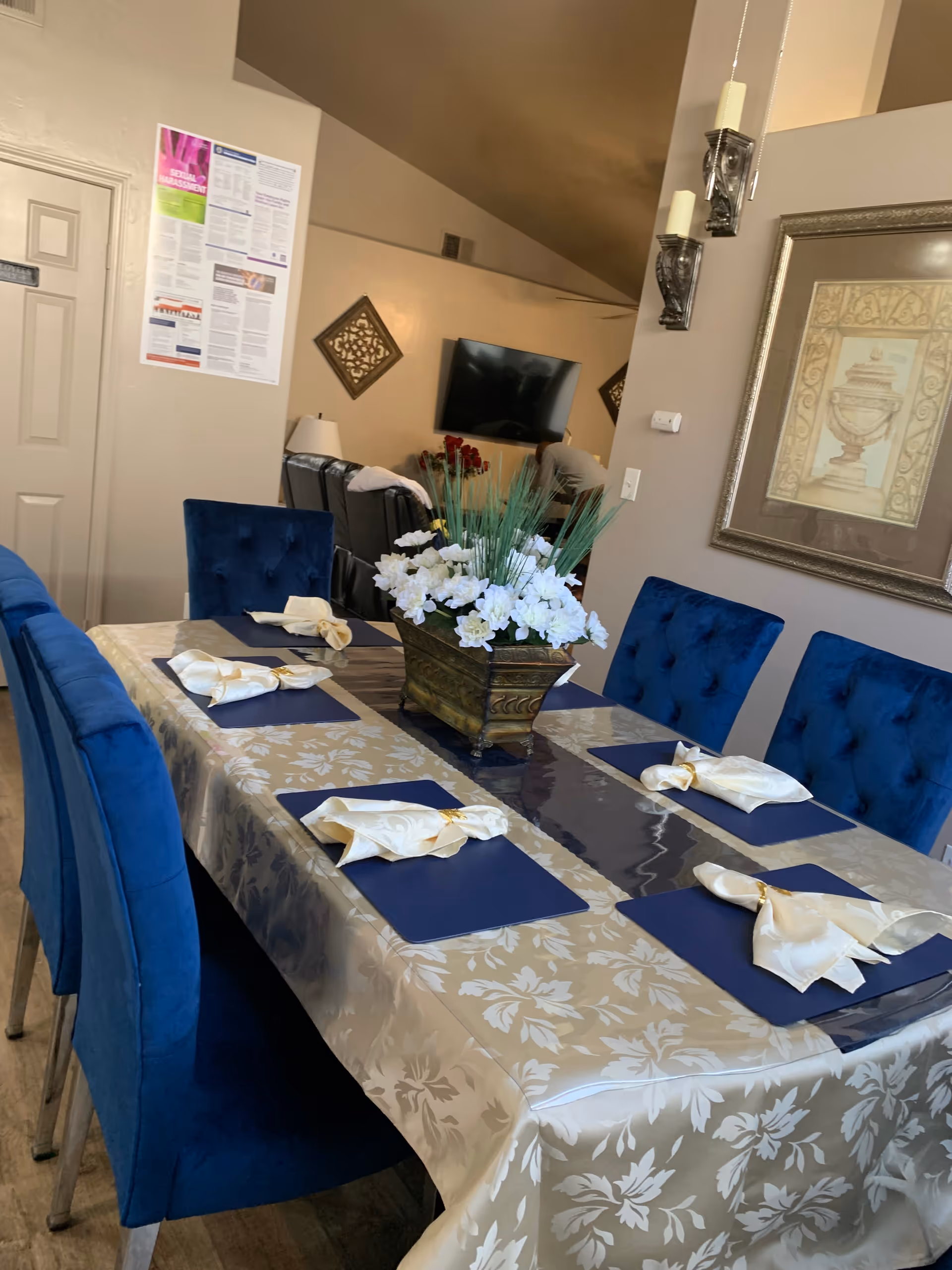 A dining room table set with blue chairs, placemats, napkins, and floral centerpiece.