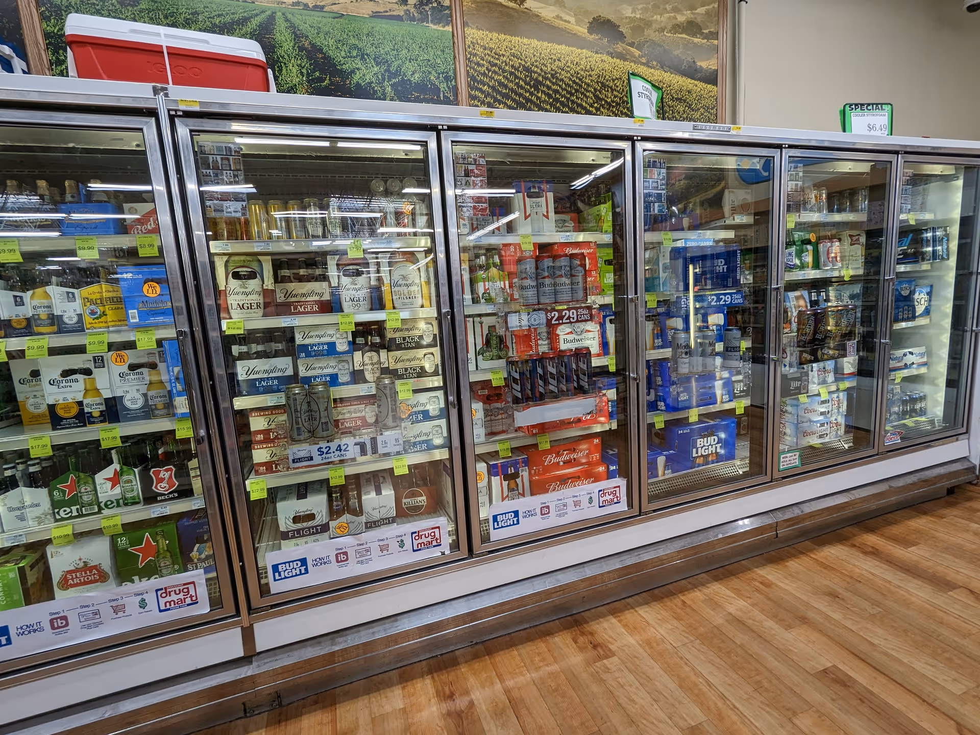 A row of glass-door refrigerated beverage coolers filled with beer and drinks inside Discount Drug Mart.