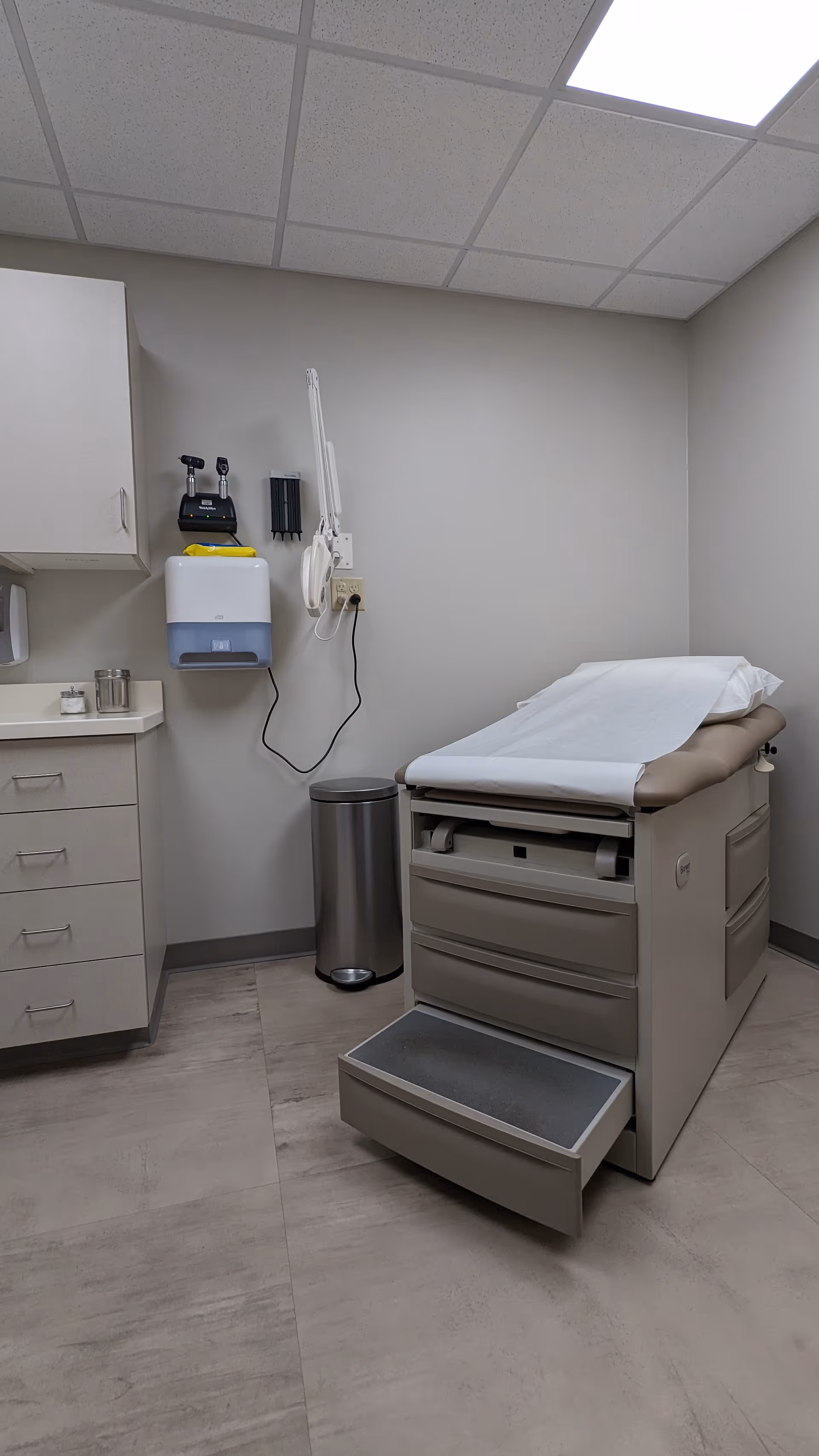 Clinical examination room with an exam table, cabinets, and wall-mounted medical equipment.