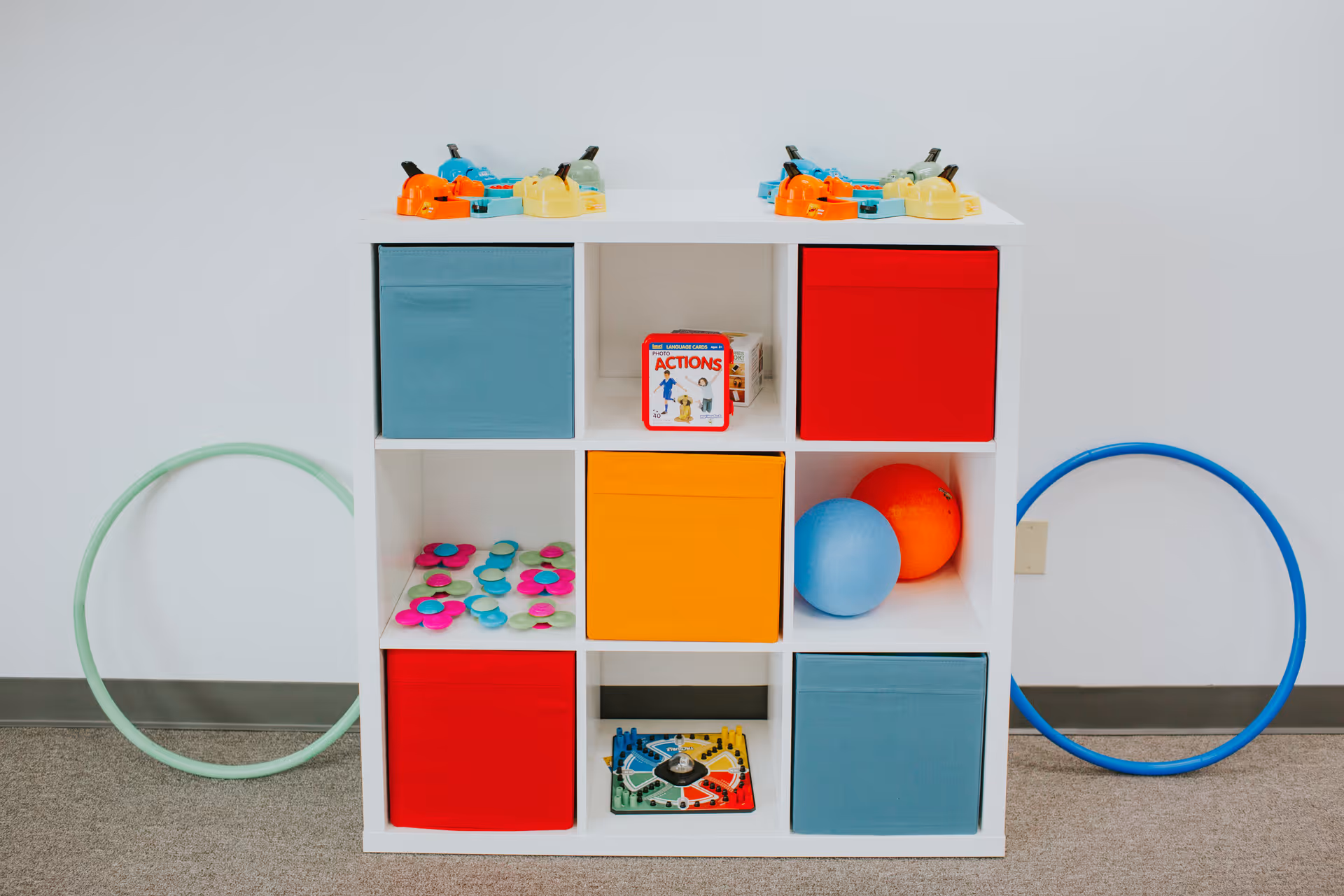 A white cubby shelving unit with colorful bins and toys in a bright play area.