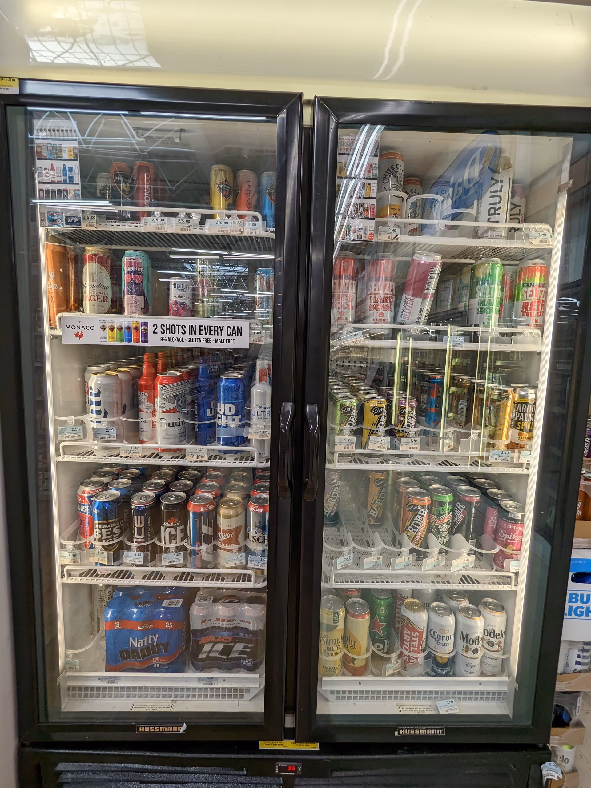 Two glass-door beverage refrigerators filled with assorted cans and bottles inside Discount Drug Mart.