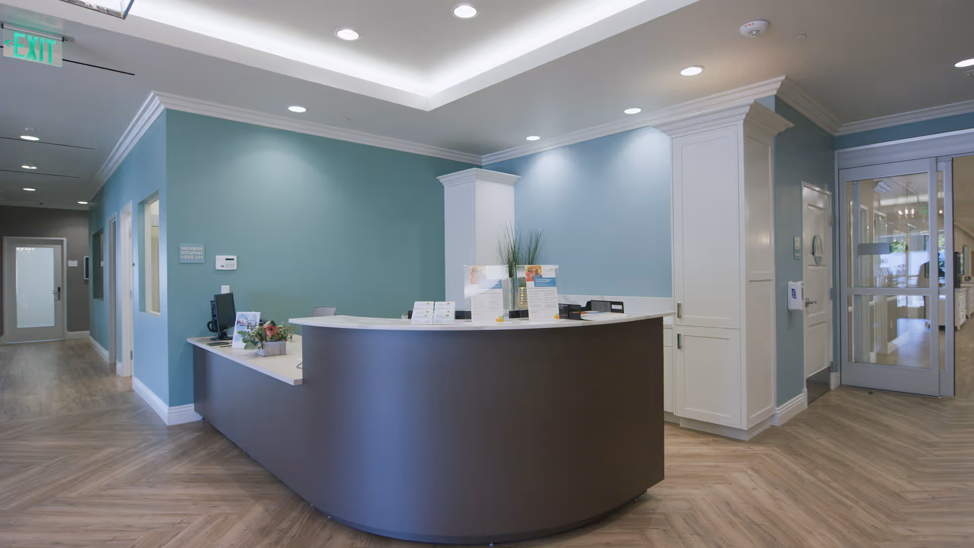 Spacious reception area with a curved dark front desk, teal walls, and glass doors.