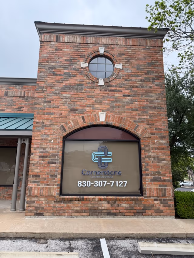 Brick building facade with round window, Cornerstone Caregiving sign, and phone number.